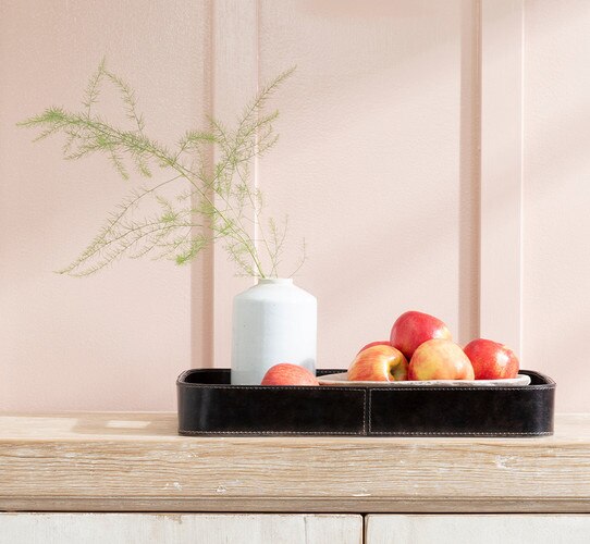 Leather tray holding bowl of apples and a white vase