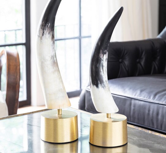 Two horn sculptures sitting on a metal base on a metal coffee table