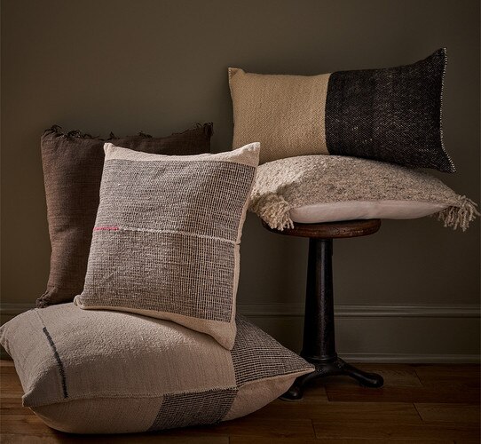 A pile of multicolored pillows sitting beside a wood stool