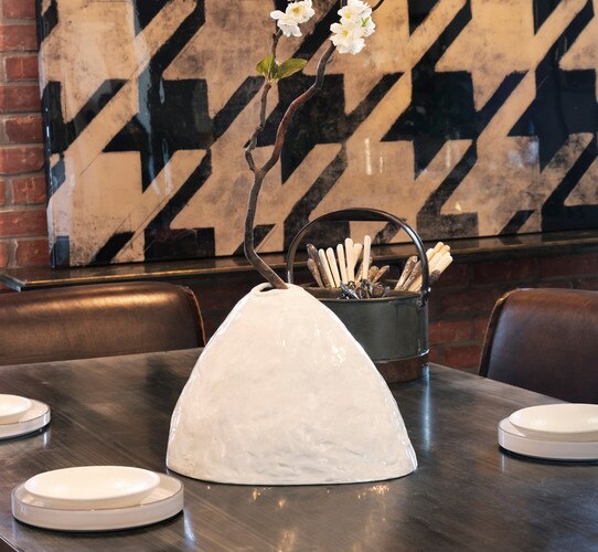 White ceramic vase holding branch with flowers on a wooden dining table