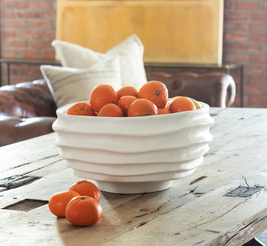 White metal bowl holding clementines on a wooden dining table