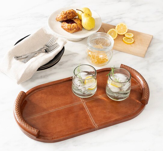 Leather tray holding two glasses of lemon water beside a plate of pastries and pears