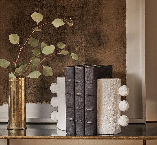 White metal bookends holding up three leather books on a metal console table