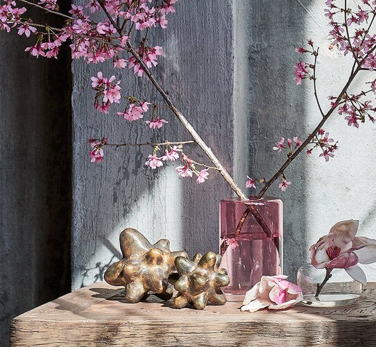 Two different sized brass sculptures beside a pink vase