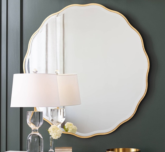 Scalloped edge gold mirror hung above a console table with a crystal lamp