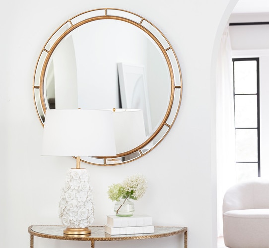 Circular gold beveled mirror above a lamp and books