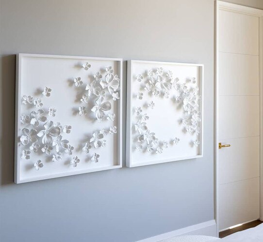 Two white ceramic flower picture frames on a gray wall