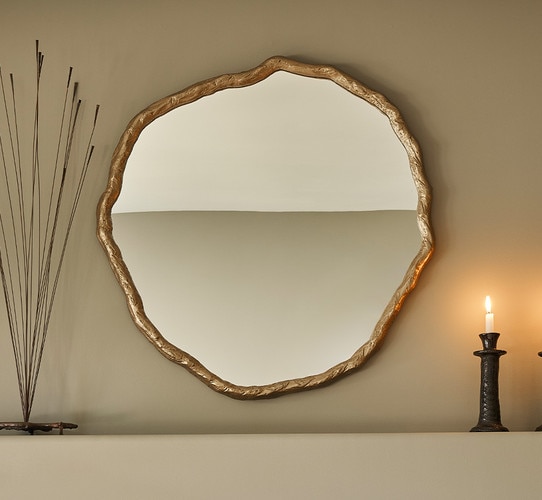Organically edged gold mirror on a mantle beside a candlestick