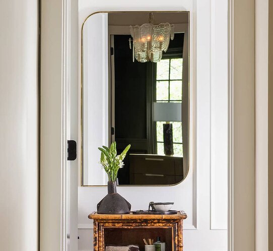 Gold mirror at the end of a hallway above a side table