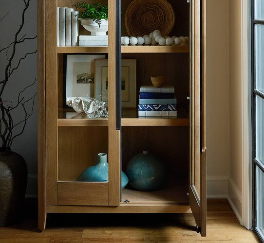 Wood cabinet with glass front holding books and décor