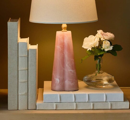 White books holding a pink lamp and clear vase with flowers
