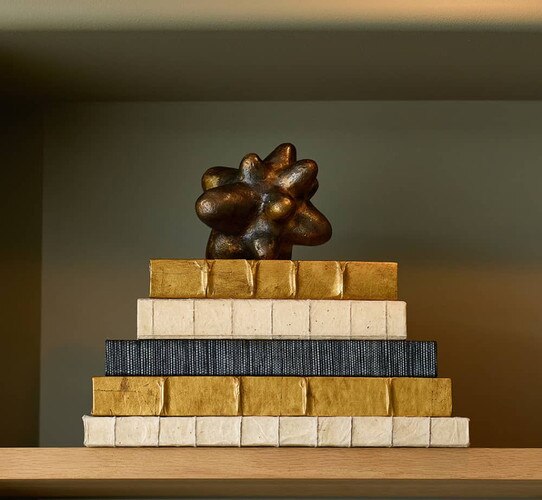 Gold white and black decorative books with a brass decorative object on top