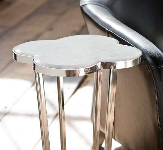 Clover shaped polished nickel side table beside a black leather chair