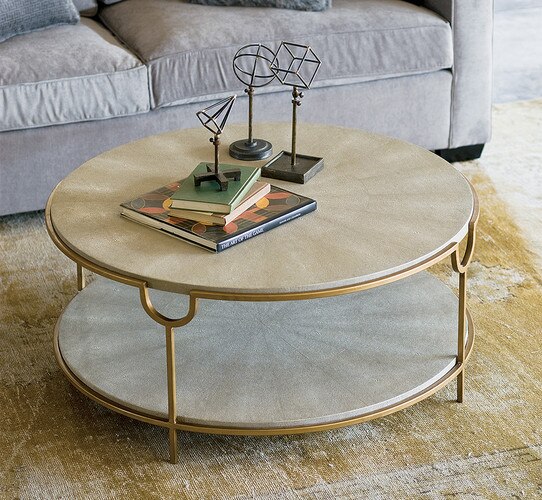 Circular shagreen table with brass legs in front of a gray couch