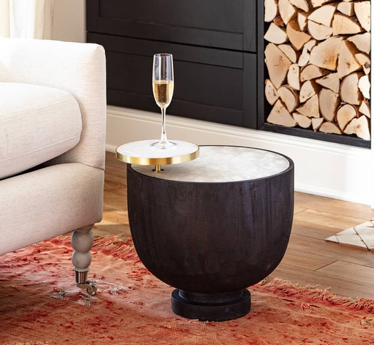 Black and brass side table holding a champagne glass next to a white sofa