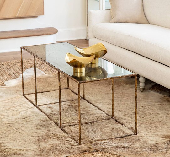 Gold coffee table holding two brass bowls next to a white sofa