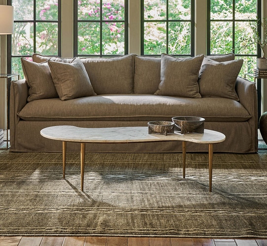 Marble coffee table holding two marble bowls in front of a green sofa