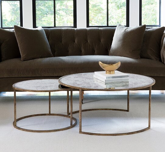 Nesting circular metal tables in front of a velvet green sofa