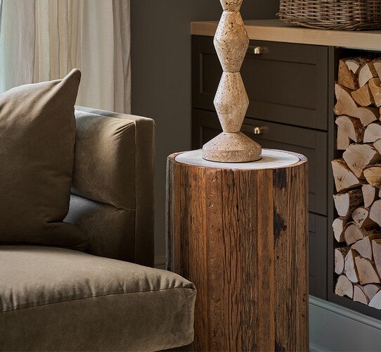 Wood side table with marble top holding a travertine table lamp next to a green sofa