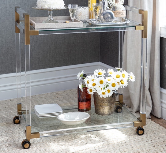 Acrylic and brass bar cart holding cake and liquor bottles