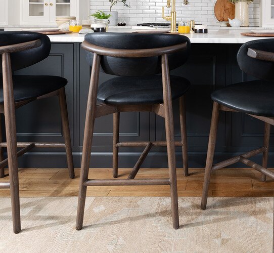 Black leather kitchen stools with wood legs next to a kitchen island