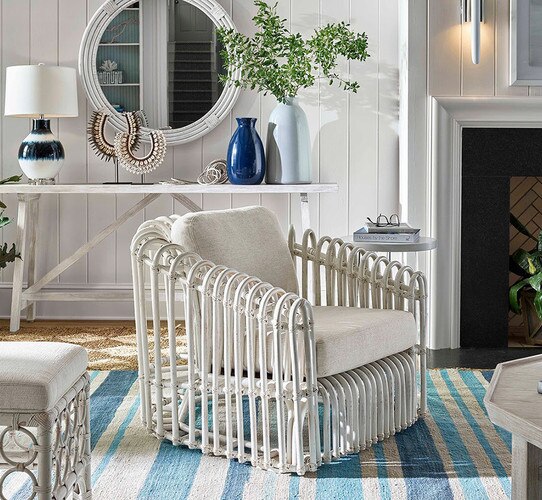 White rattan chair in front of console table with lamps and vases