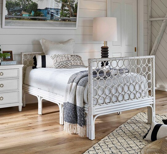 White rattan day bed beside a floor lamp and side table