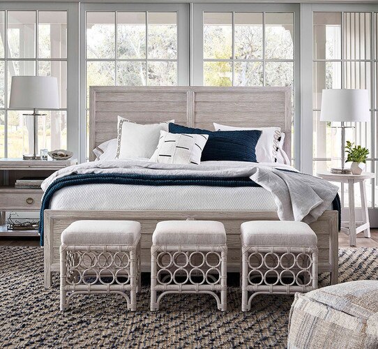 Bedroom with large white wood bed and three rattan stools at the foot
