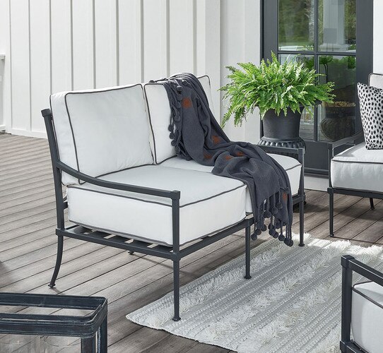 Black metal loveseat on a patio with a gray throw blanket over the back
