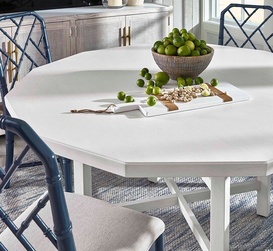 White octagonal dining table with blue chairs around it and a jar of limes on top