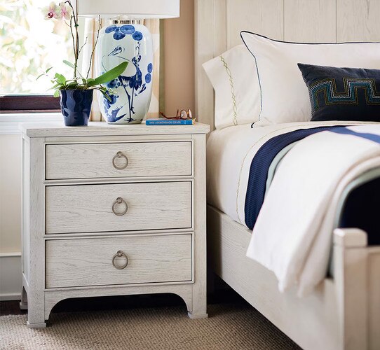 Wood nightstand with a lamp on top next to a bed