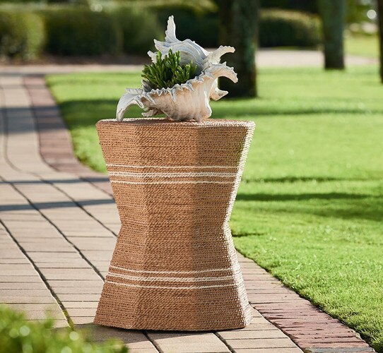 Wicker side table holding a conch shell on a brick path