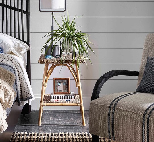 Wicker side table holding a lamp and plant next to a bed