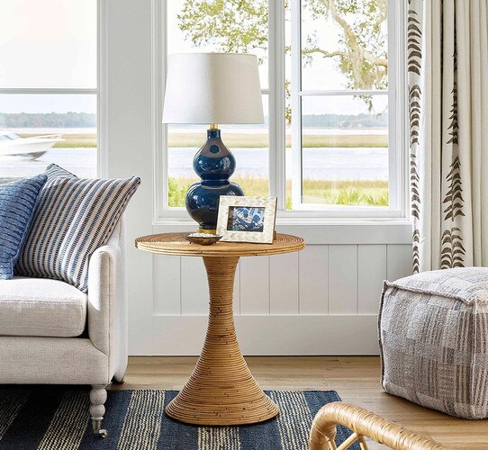 Rattan side table holding a navy lamp next to a sofa