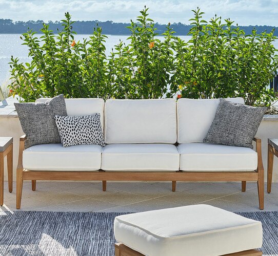 Wood sofa with white cushions on a patio in front of a lake