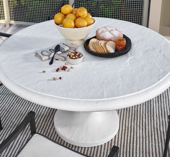 White concrete outdoor table holding a bowl of fruit and a plate of bread