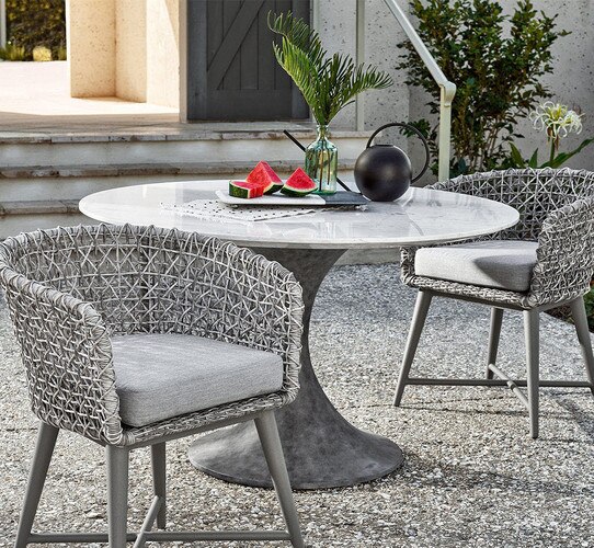 Circular outdoor dining table with two chairs and a plate of watermelon on top