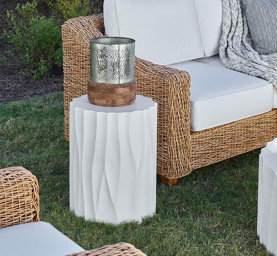 White textured side table next to a wicker sofa on a lawn