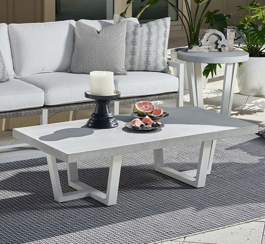 Long concrete coffee table holding two plates of grapefruit and a candle on a patio