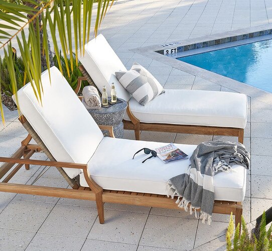 Two wood and linen chaise lounges beside a pool