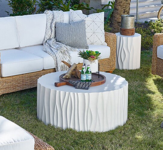 Circular white concrete coffee table holding a wood serving tray holding bottles of water