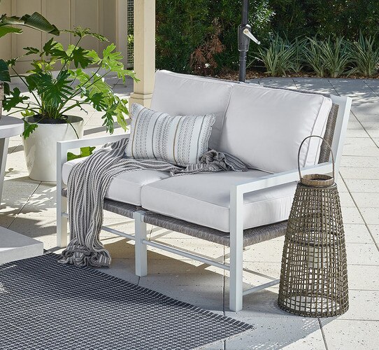 White and wicker loveseat on a patio beside a woven hurricane