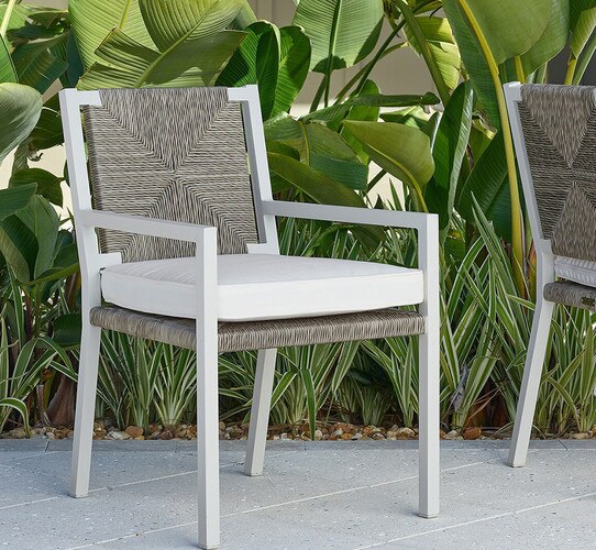 White and gray woven outdoor chair on a patio in front of greenery