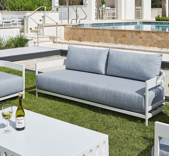 White and linen outdoor sofa in front of a pool