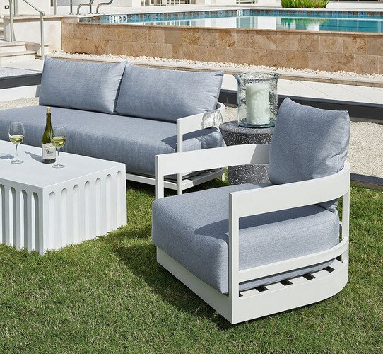 Outdoor sitting area with a sofa a chair and a white coffee table holding wine glasses