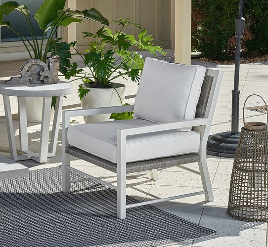 White and woven chair on a patio beside an umbrella and side table