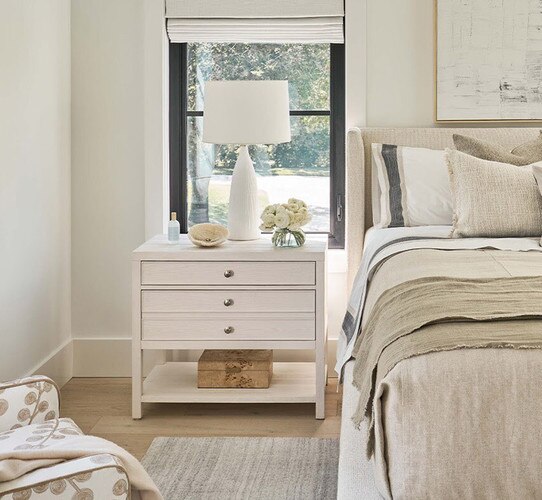 Wood nighstand holding a white lamp in front of a window