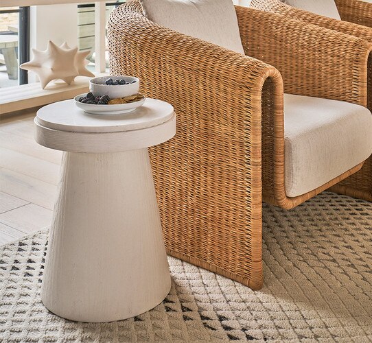 White wood side table holding snack bowl beside a rattan accent chair