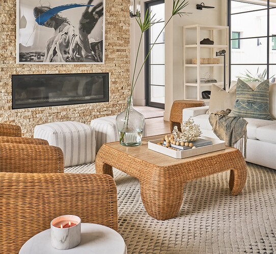 Living room with woven coffee table, linen stools, and a large stone fireplace