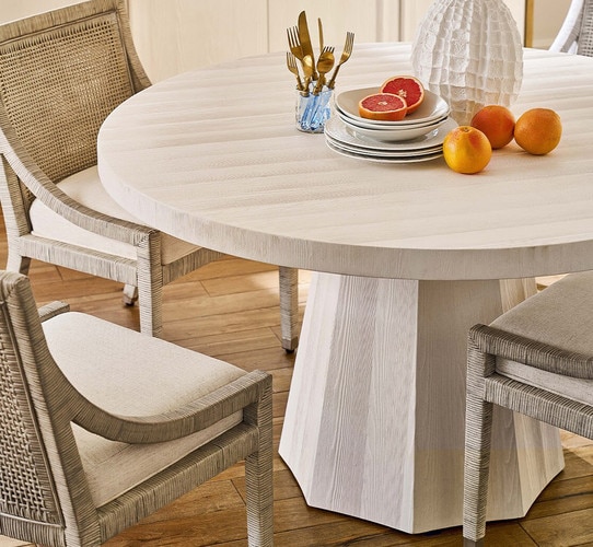 Circular wood dining table holding fruit and gold silverware